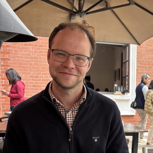 A white man wearing glasses in a smart outfit smiles.